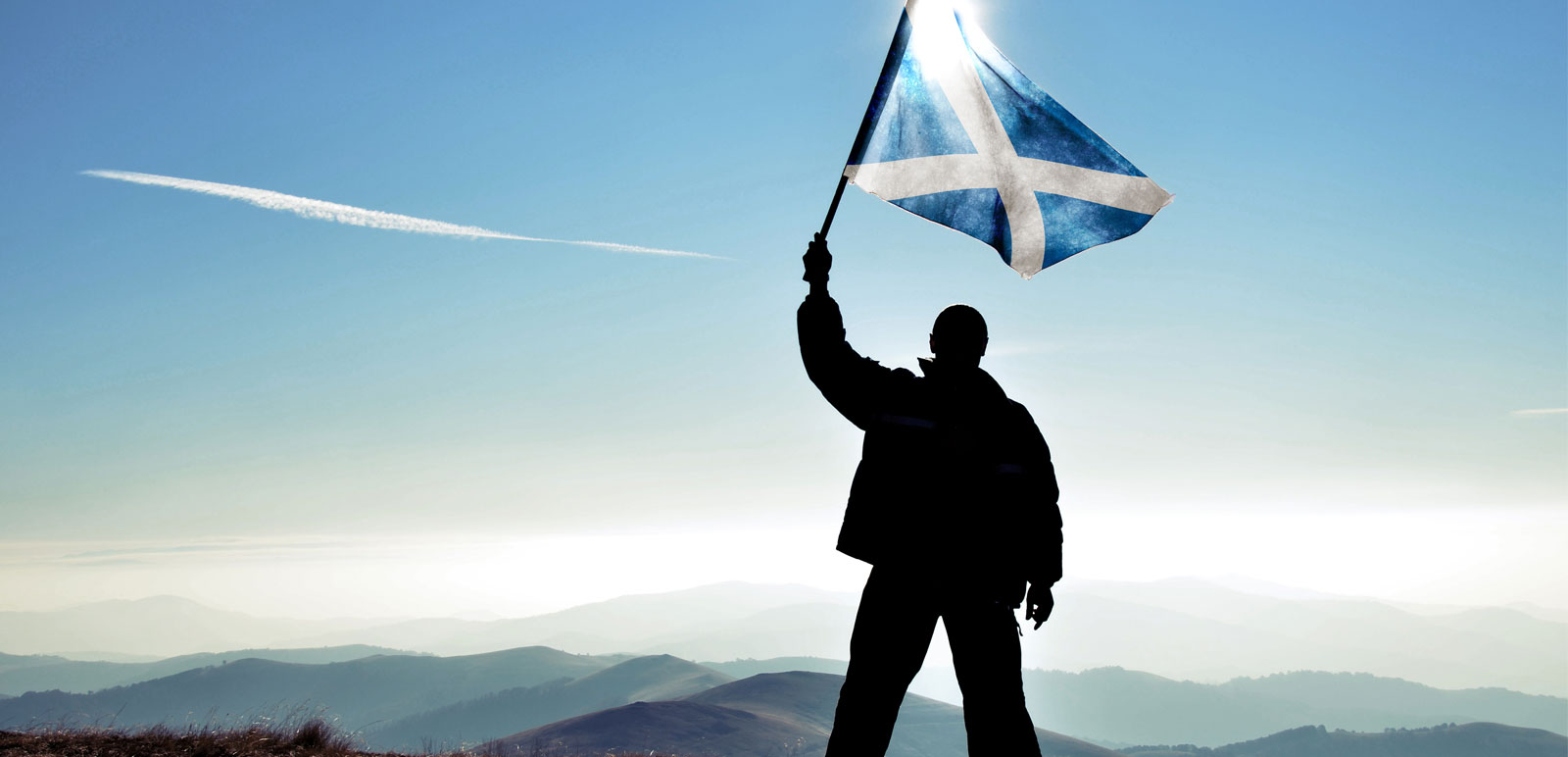 man waving a scotland flag on a mountain top