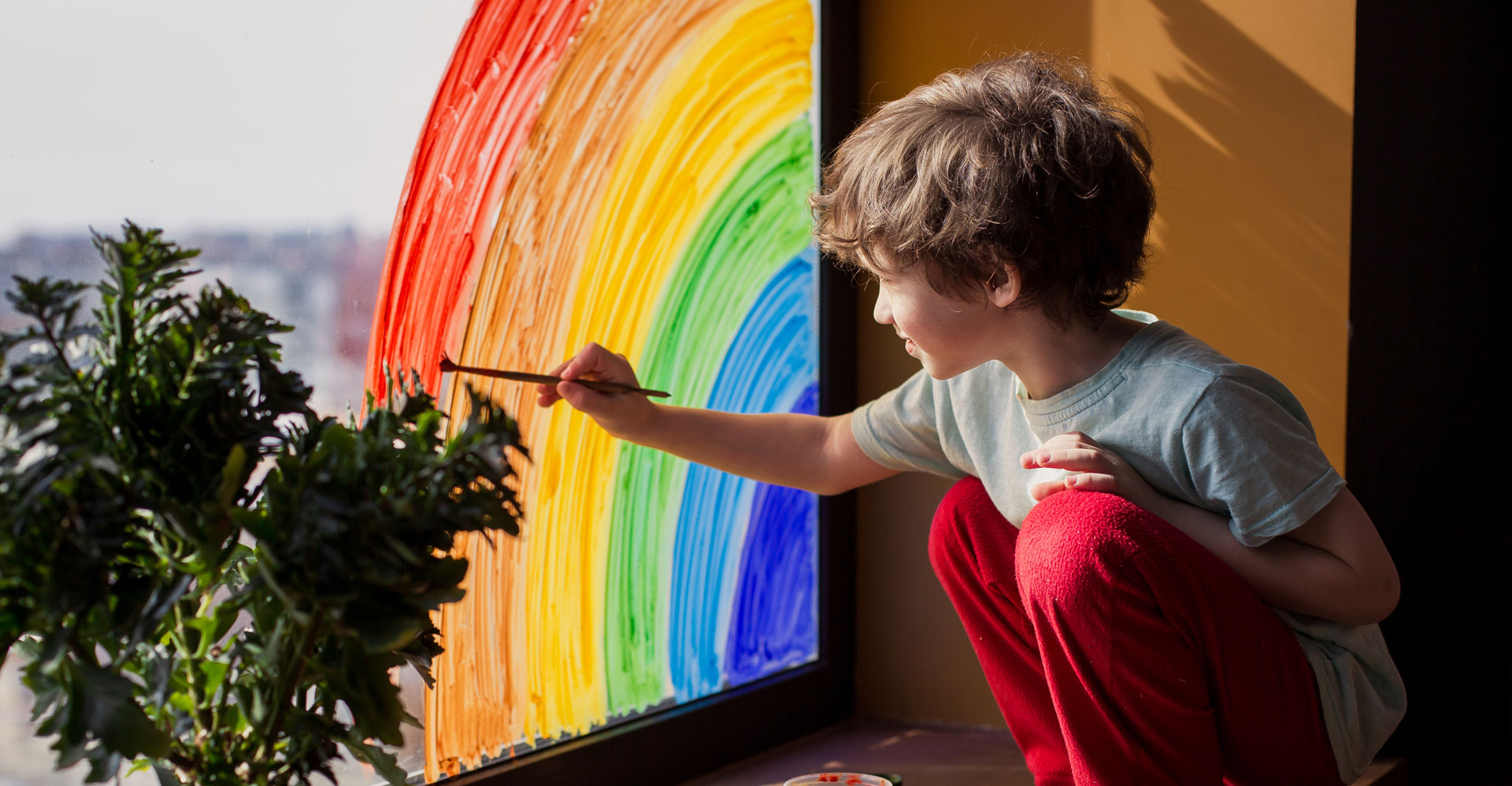 boy painting a rainbow on a window