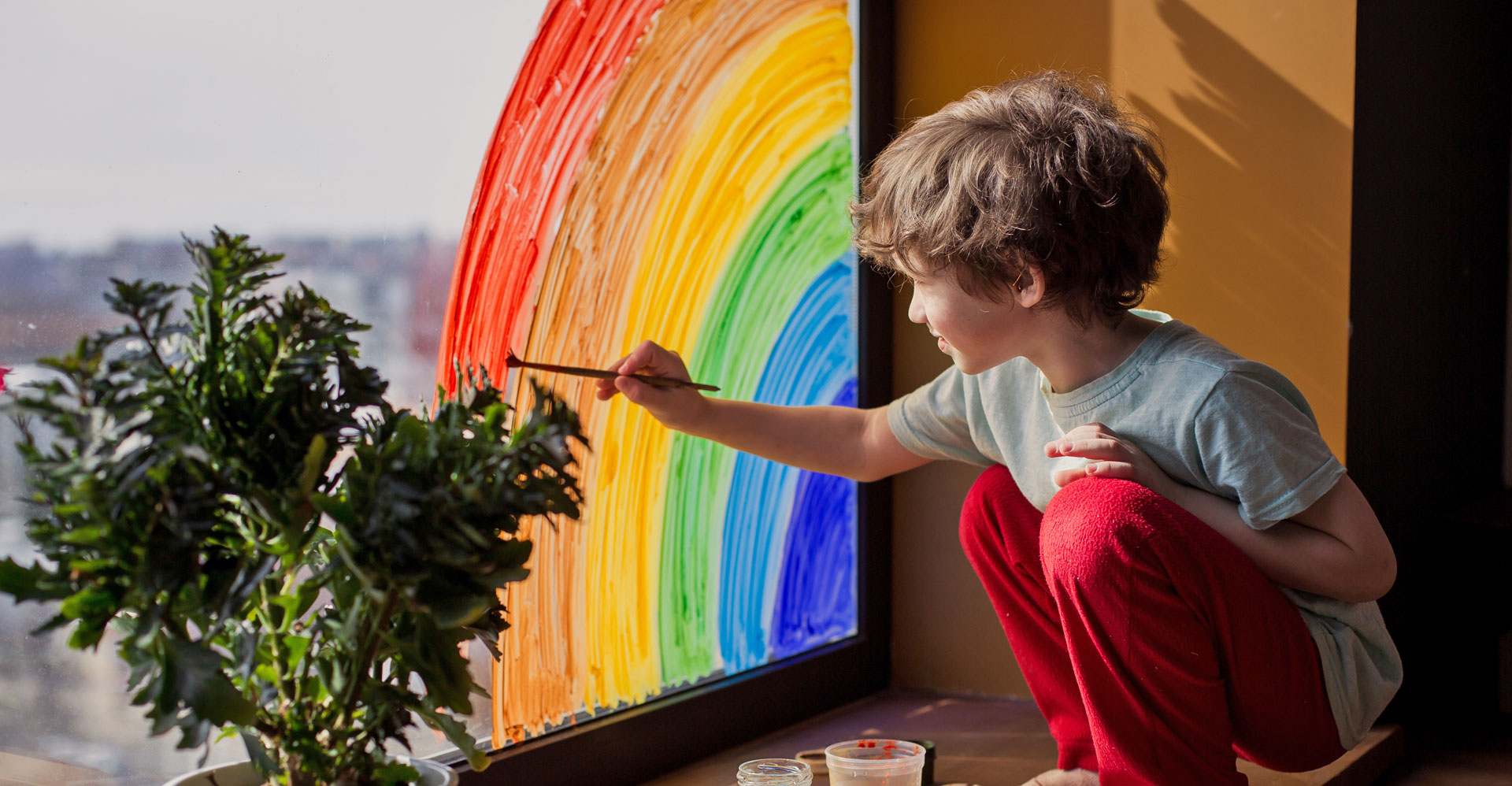 boy painting a rainbow on a window