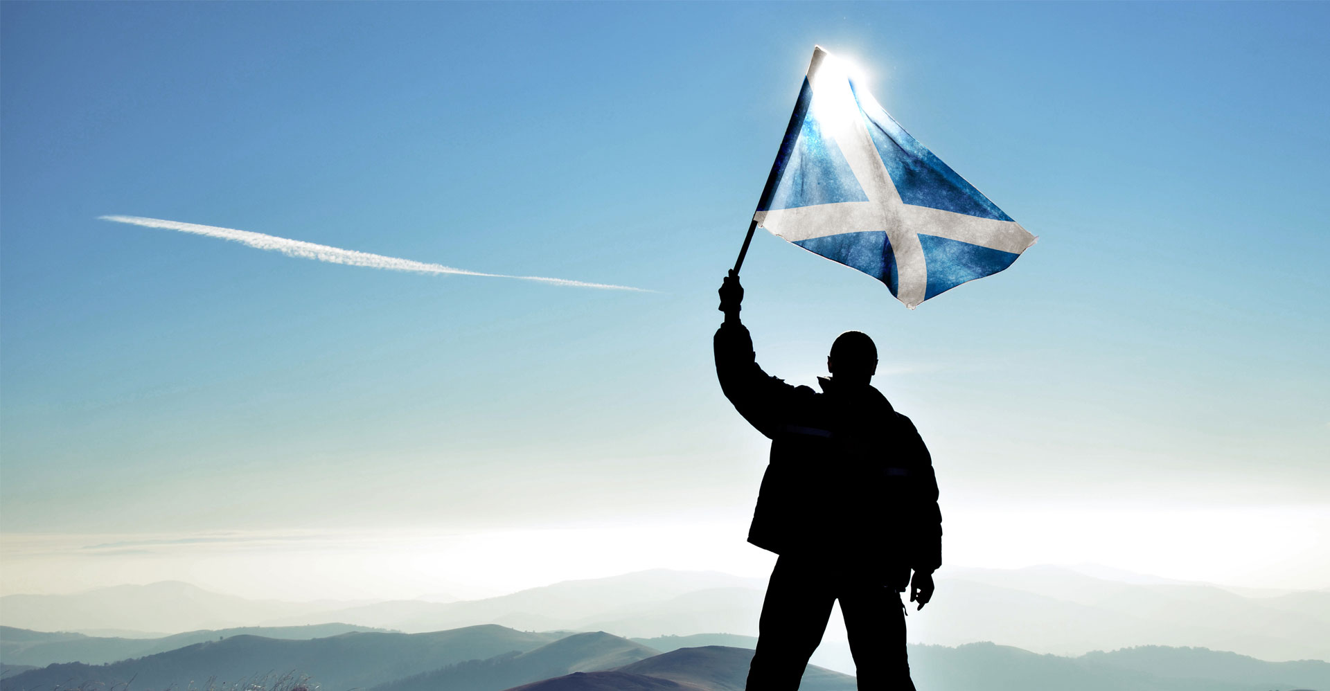 Man waving a Scotland flag on a mountain top