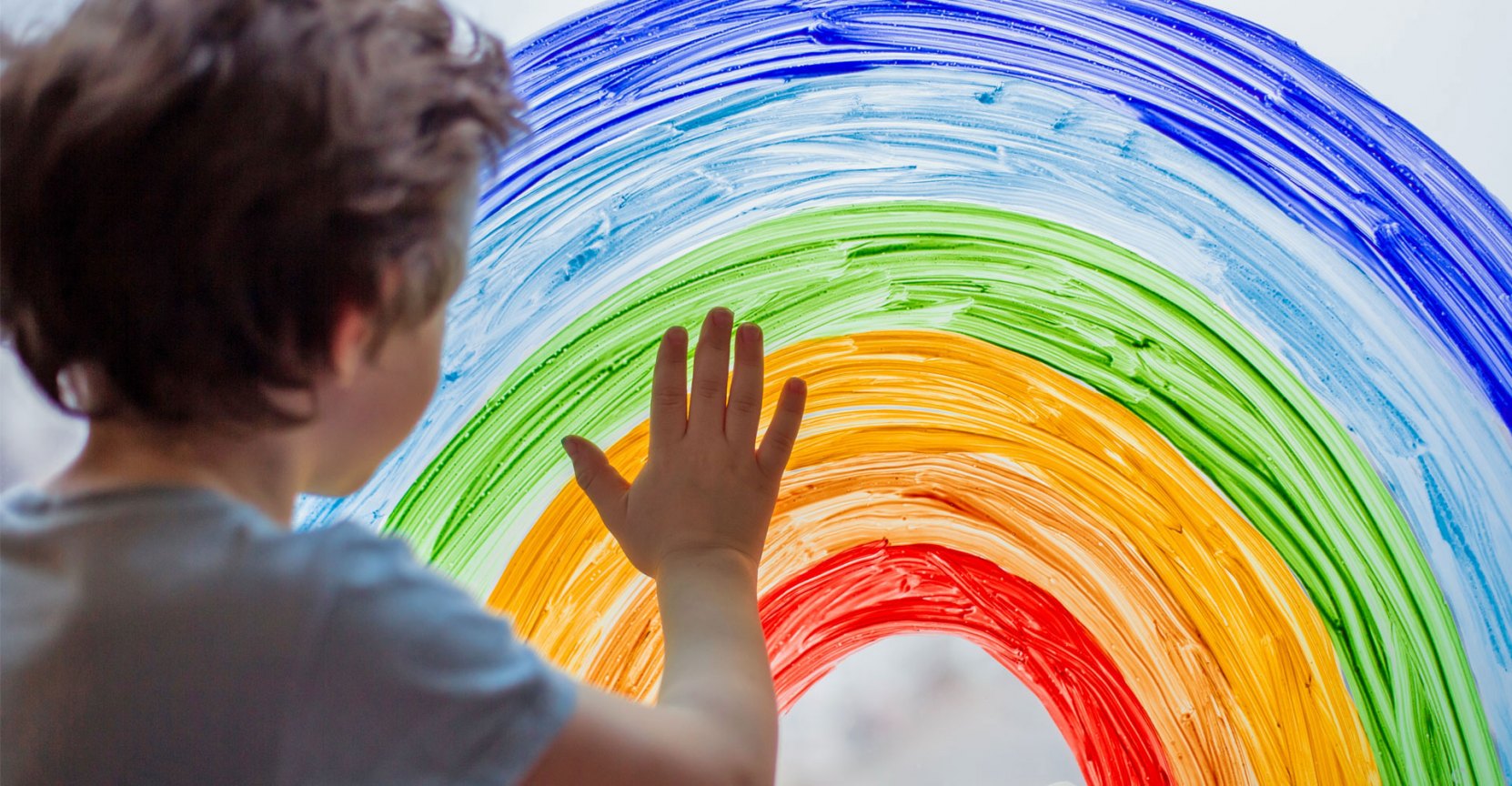 boy painting a rainbow on a window