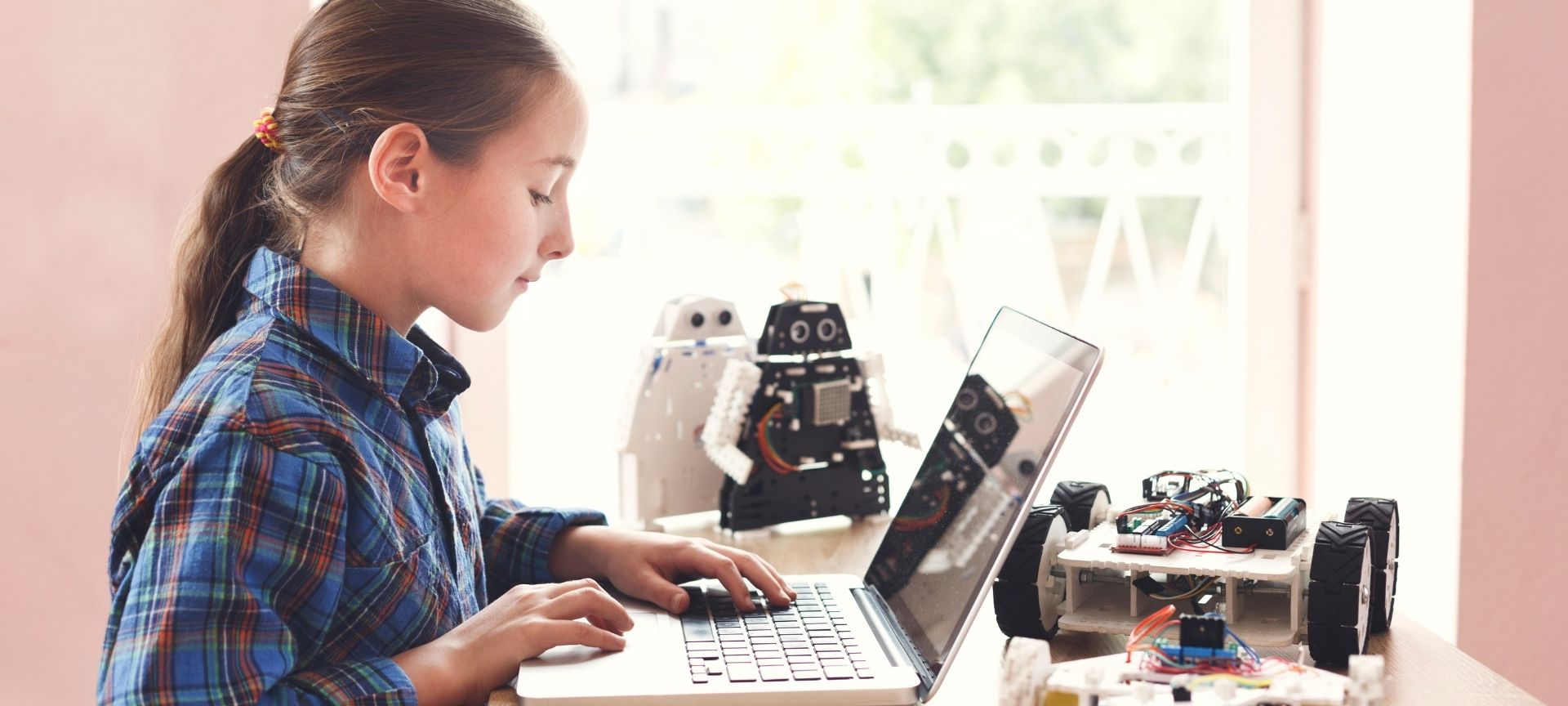 young girl using computer with robots in front of her