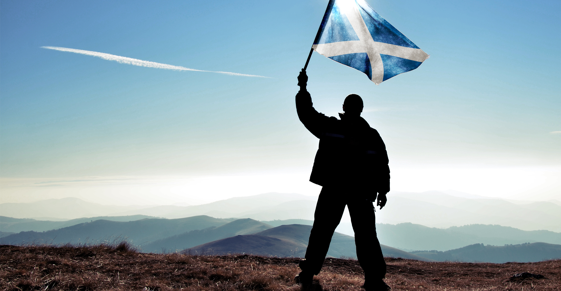 man on mountain waving a Scotland flag