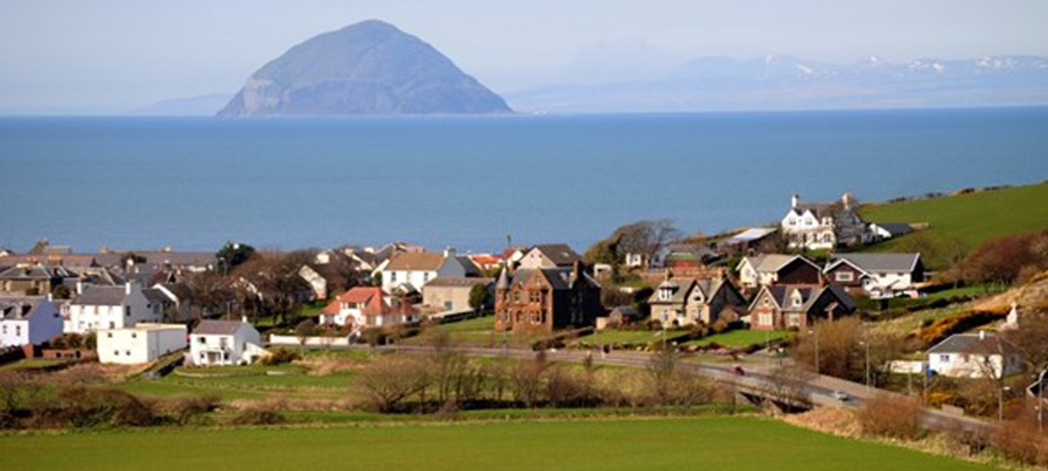 A sunny view of a collection of houses in front of a body of water with a small island in the background