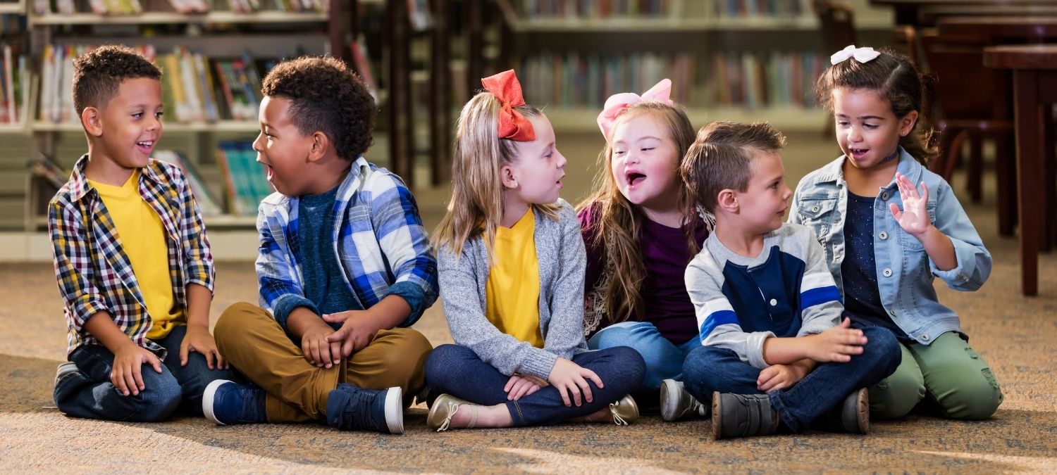 A diverse group of children sit together smiling in a library