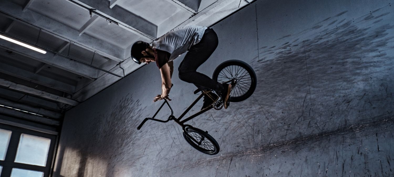 A young man wearing on a helmet is on a BMX bike performing an air jump indoors