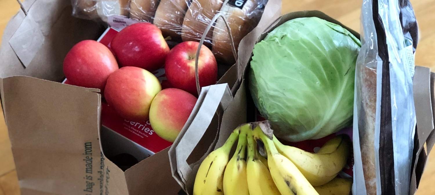 A box containing a variety of fruit and vegetables including bananas, apples and a cabbage