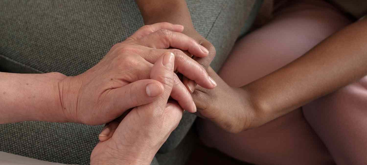 Two pairs of women's hands showing one offering comfort to the other