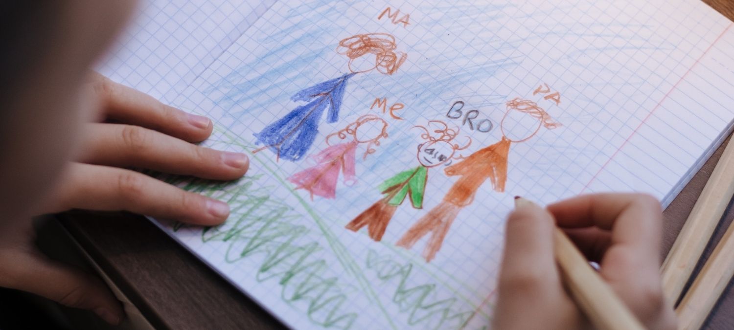 A close up of a child using colouring pencils to draw a picture of a family