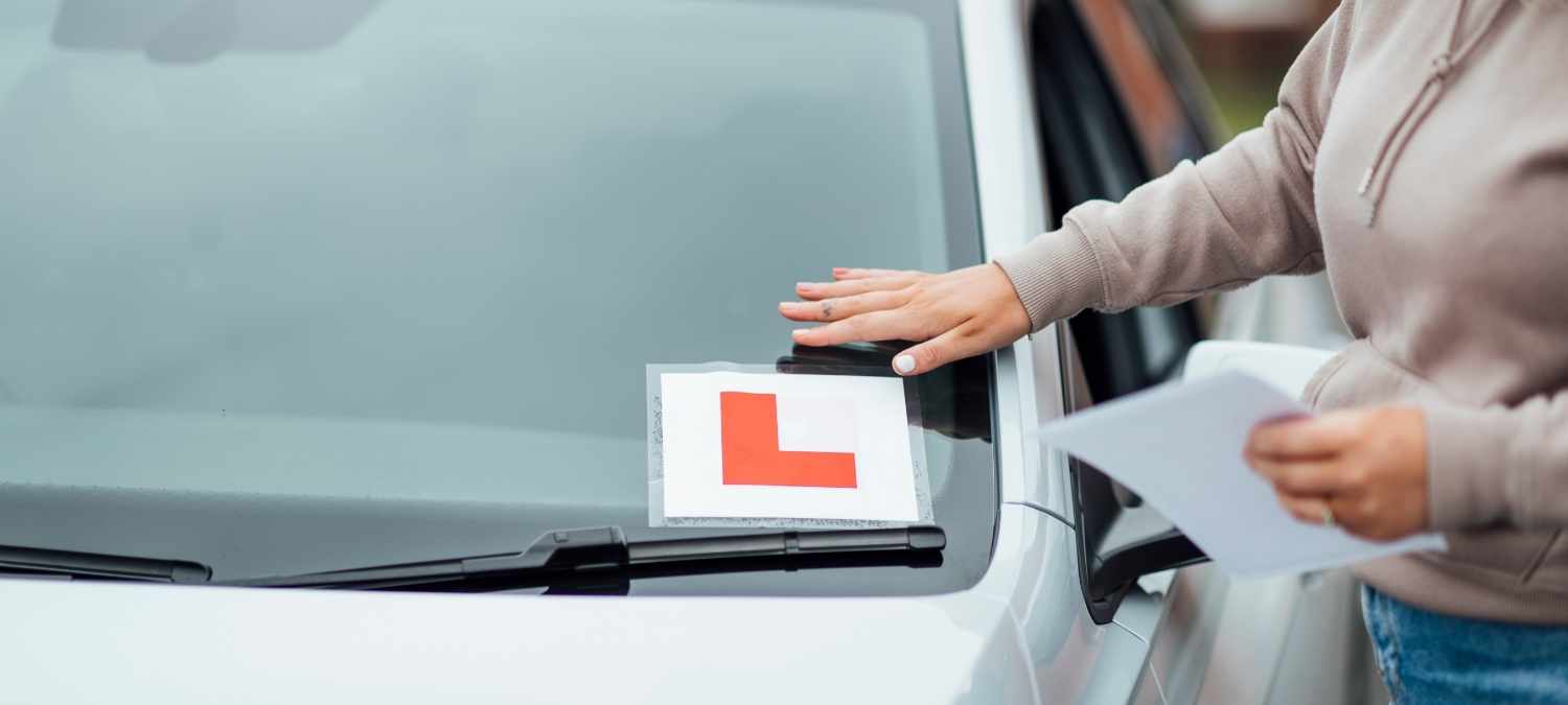 A hand placing a learner driver sticker on the front of a car