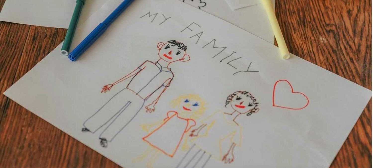A picture drawn by a child featuring a child with a mum and dad either side with the words my family written above and simple heart drawn above them