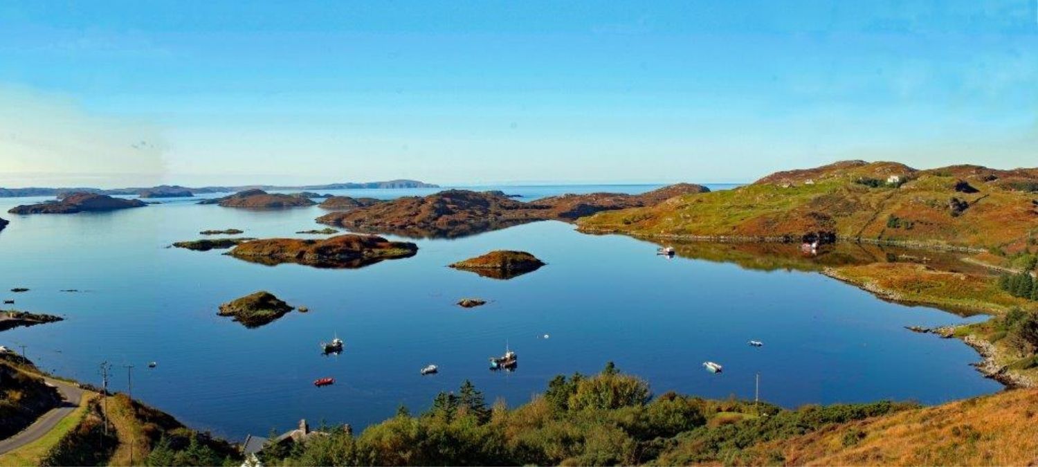 A sunny view of a collection of boats moored in water surrounded by hills