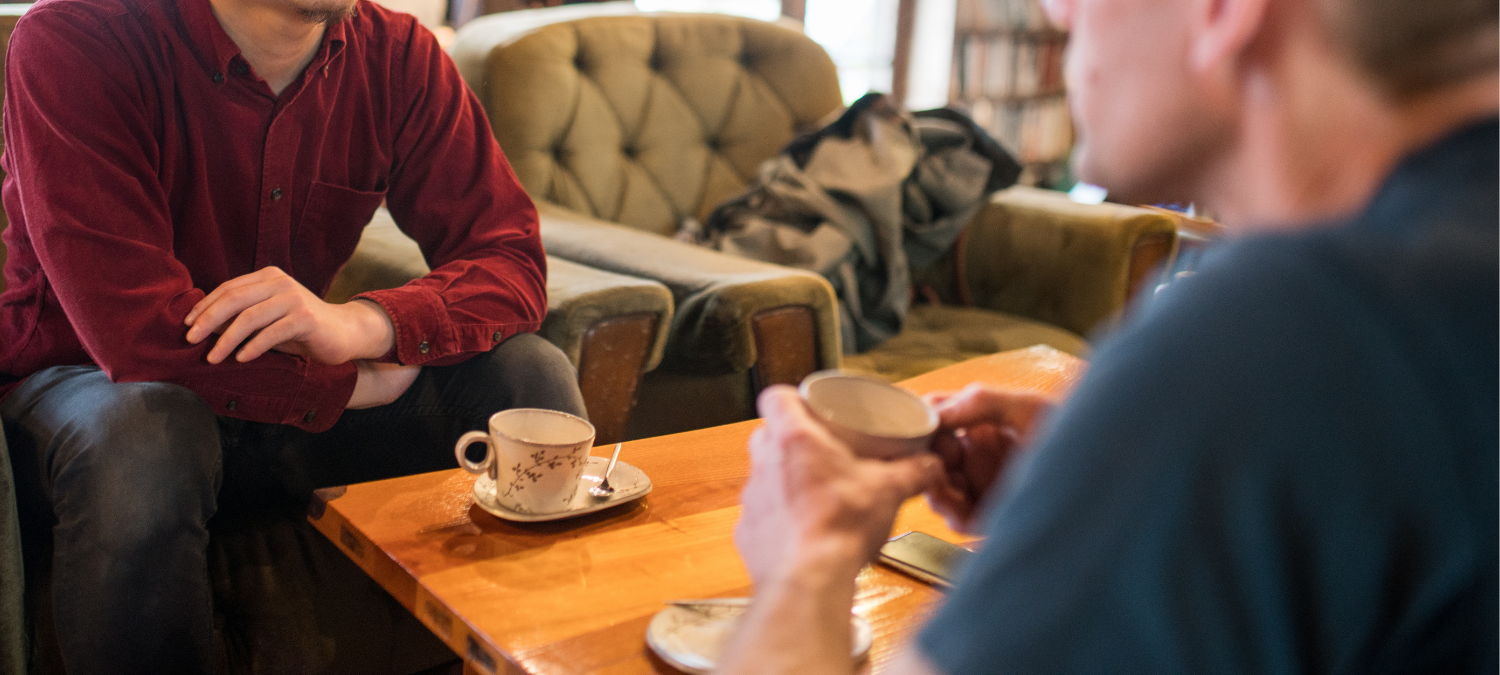 two men are talking over cups of coffee