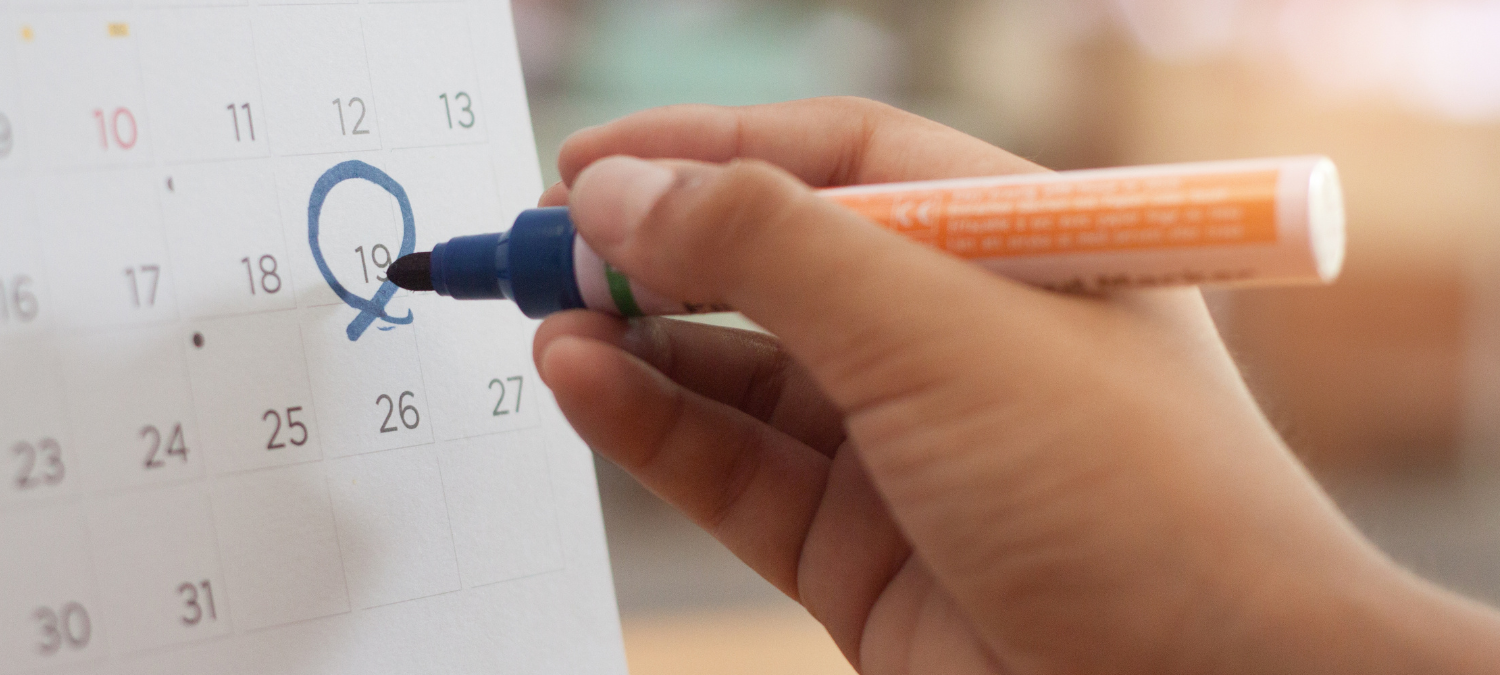 a hand holding a pen and marking a date on a calendar