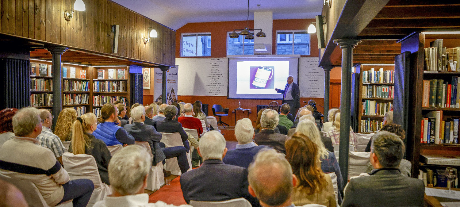 audience sitting in the library watching Sir John Timpson talk on stage