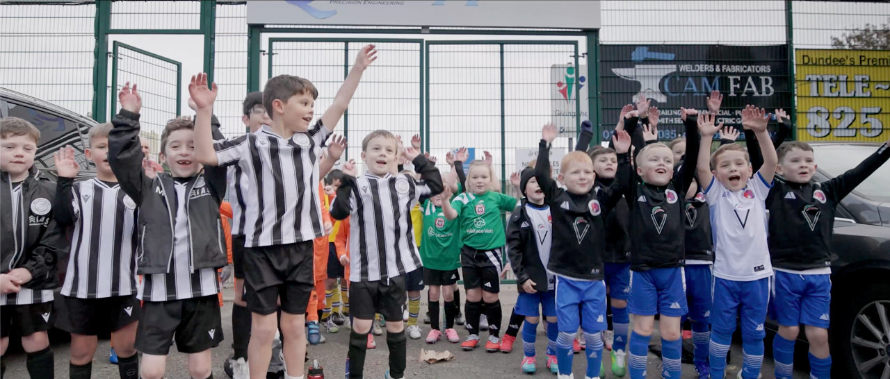 wee children in football strips with arms in air